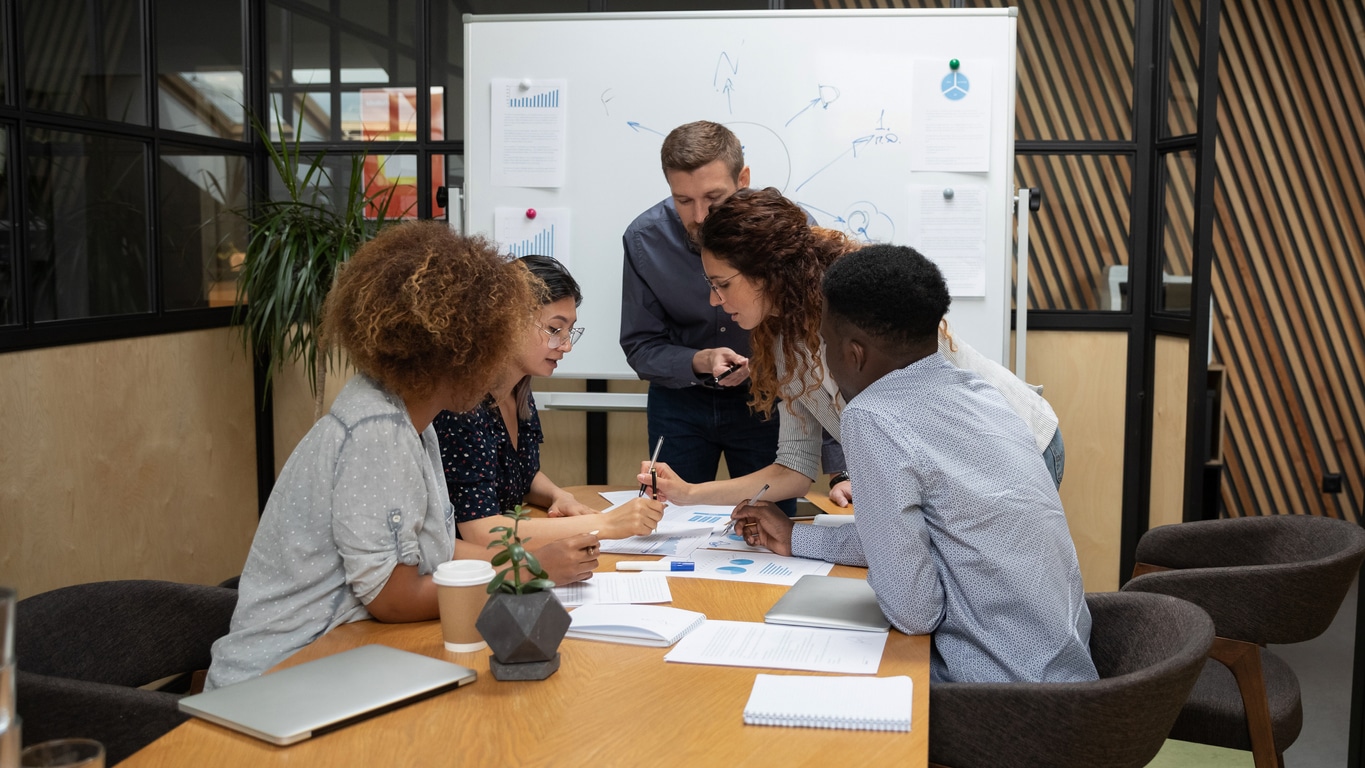 Five people are collaboratively working on a data report that is spread across the table.