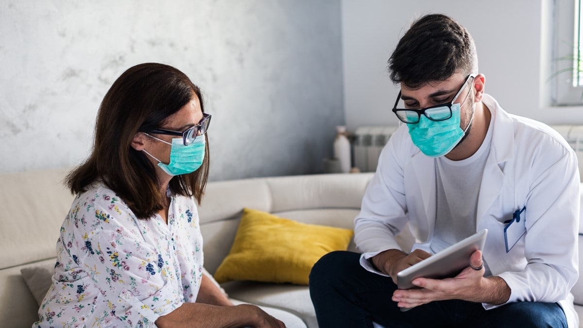 A healthcare provider sits near a woman in an office. He has a tablet in his hand to show information.