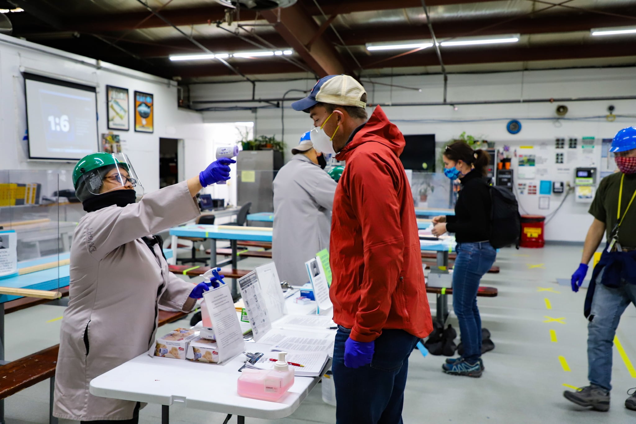 A woman dressed in PPE checking a man's temperature.