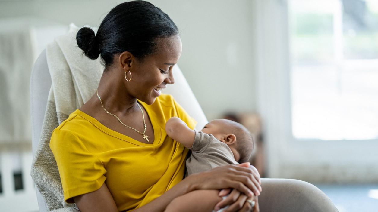 A mom sits in a chair and breastfeeds her infant