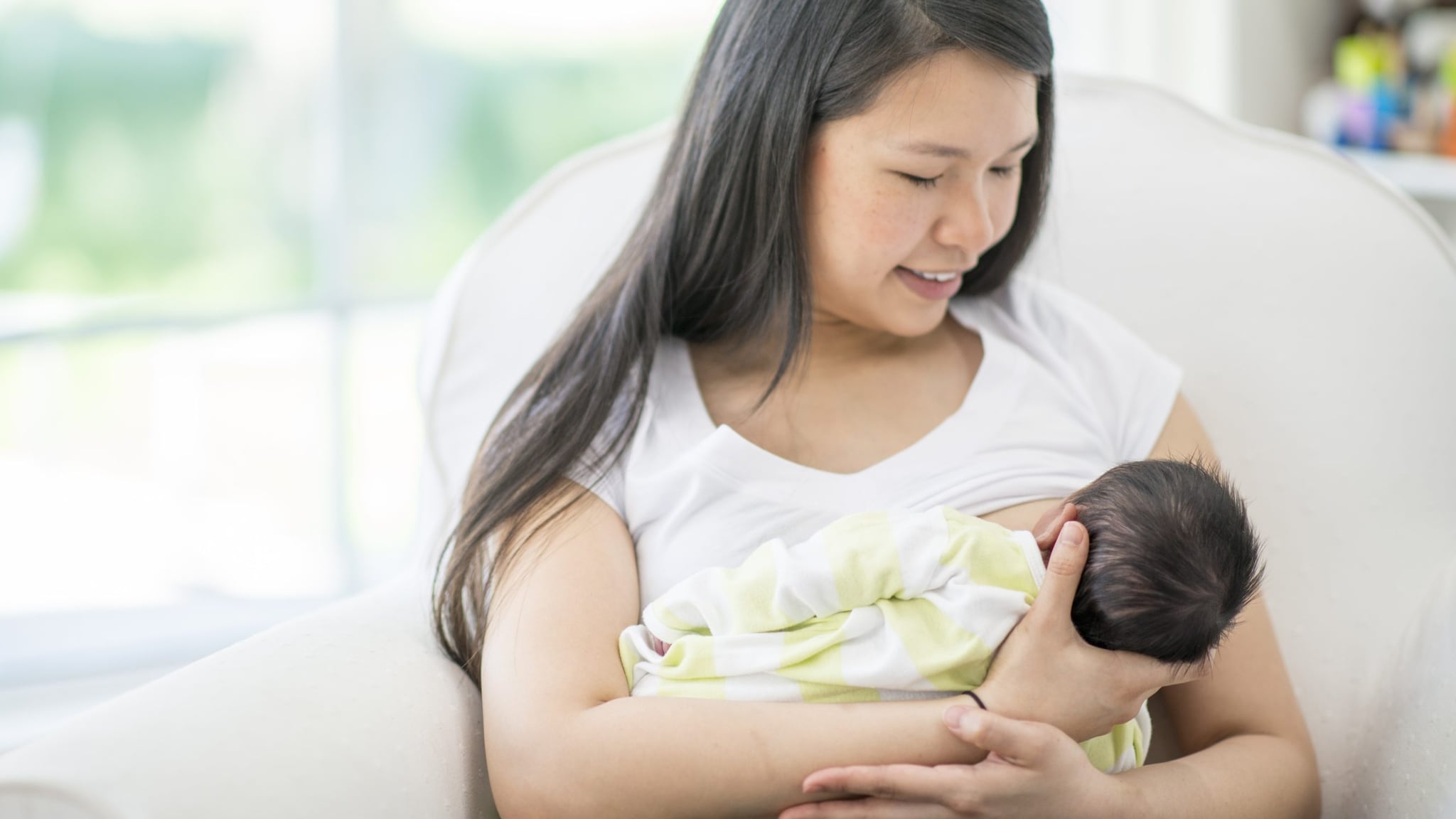 Woman breastfeeding an infant while sitting in a white chair.