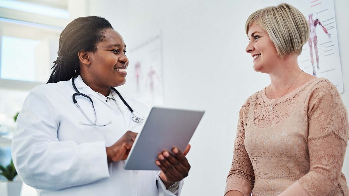 A doctor holding a computer tablet talks to a woman patient