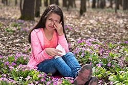 Girl with itchy eyes sitting among flowers.