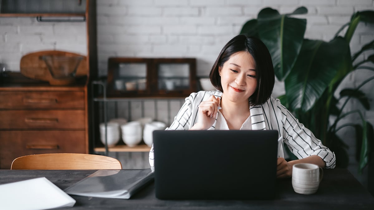 Asian woman seated, researching information on laptop computer, smiling