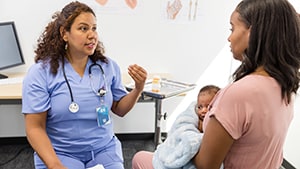 healthcare provider talking to mother who is holding infant in a doctor's office exam room