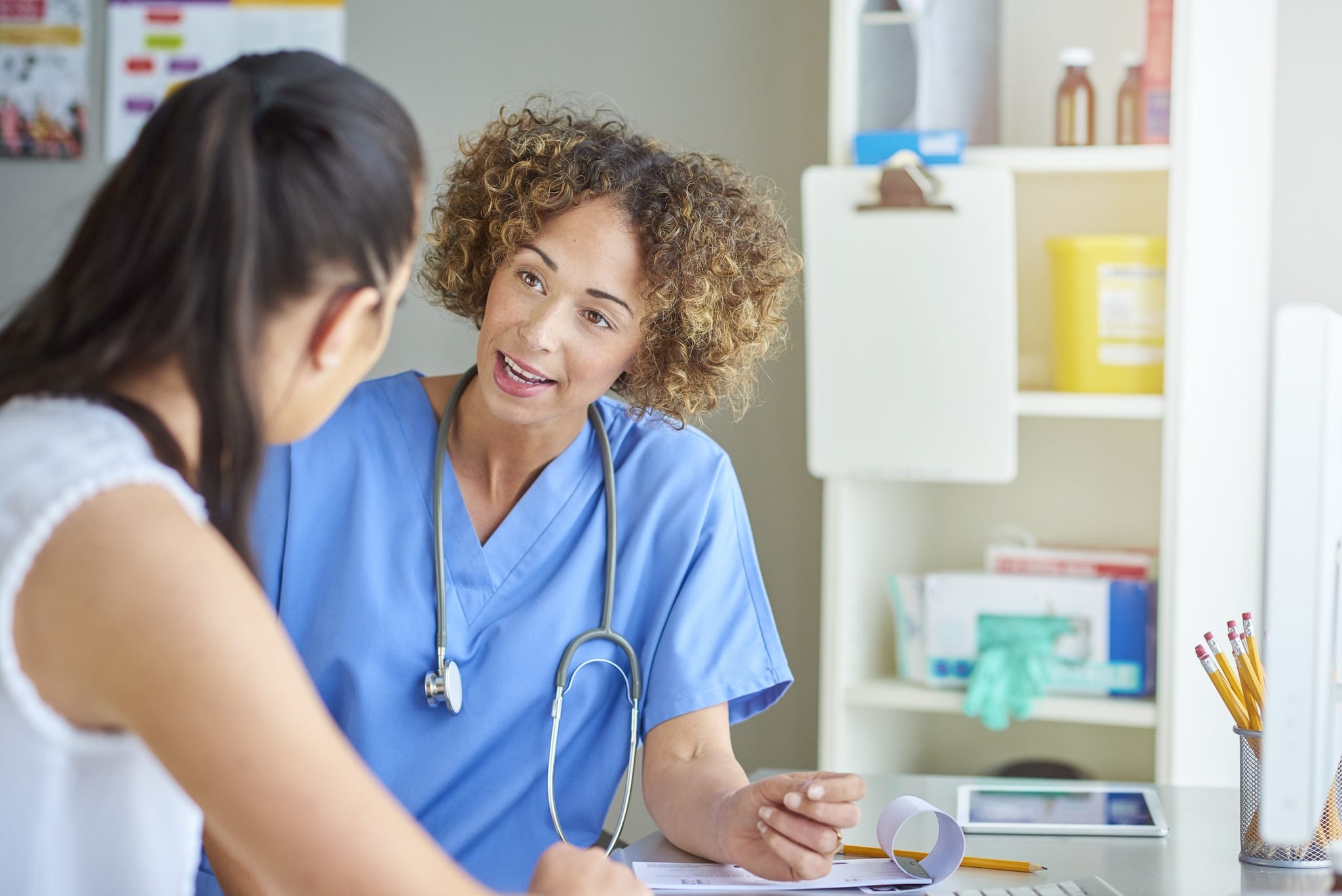 A healthcare provider speaking to a patient in an exam room.