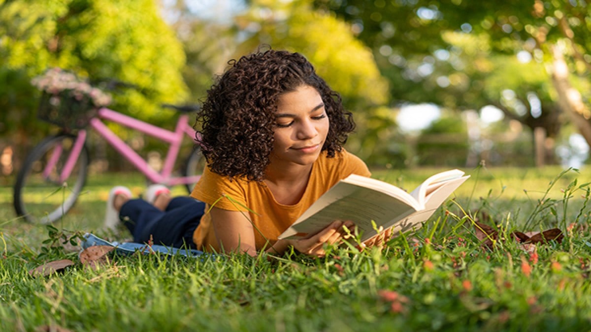 Mujer leyendo un libro acostada en el césped en un parque.