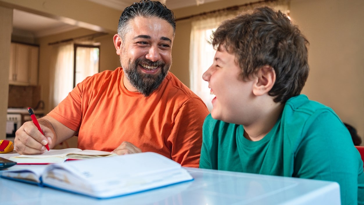 Father and son at a table with a notebook open in front of them.