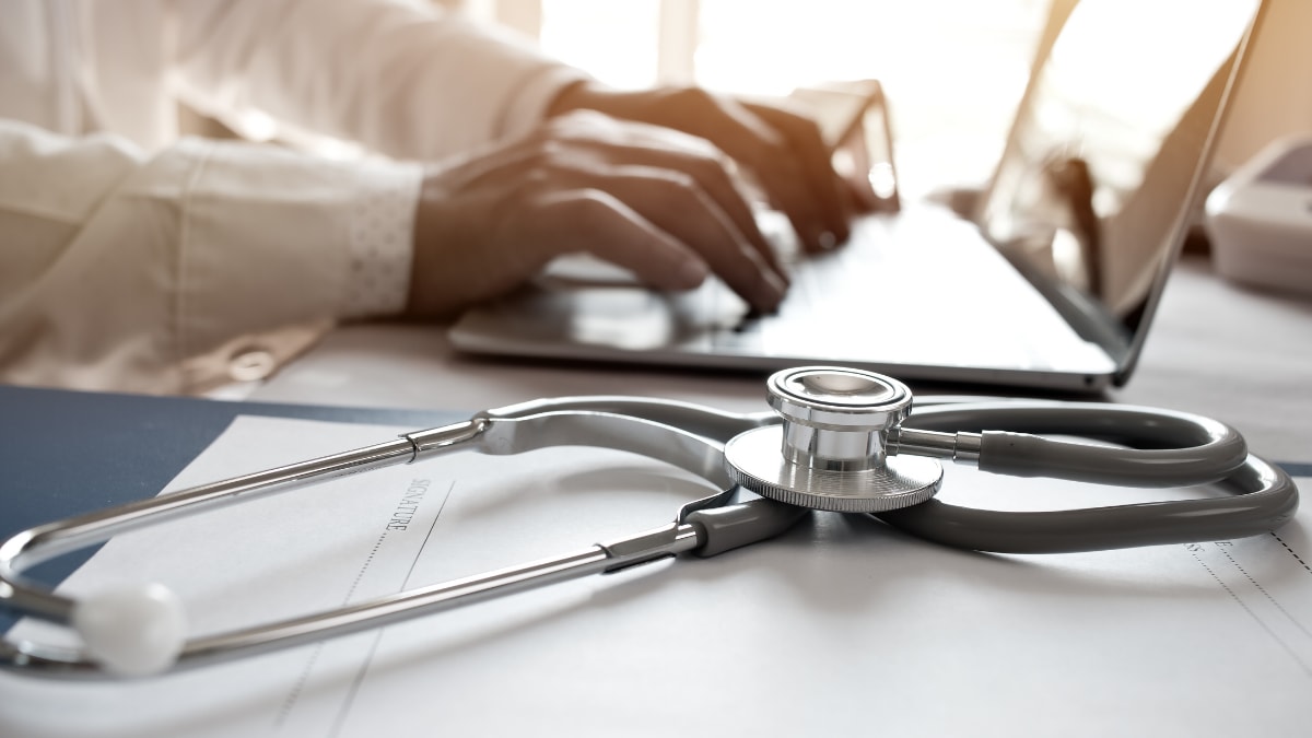 A doctor sitting at a desk with a laptop and a stethoscope.