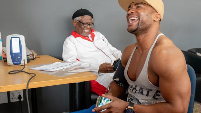 Jason sits smiling while getting blood pressure taken during assessment with a surgeon for VMMC.