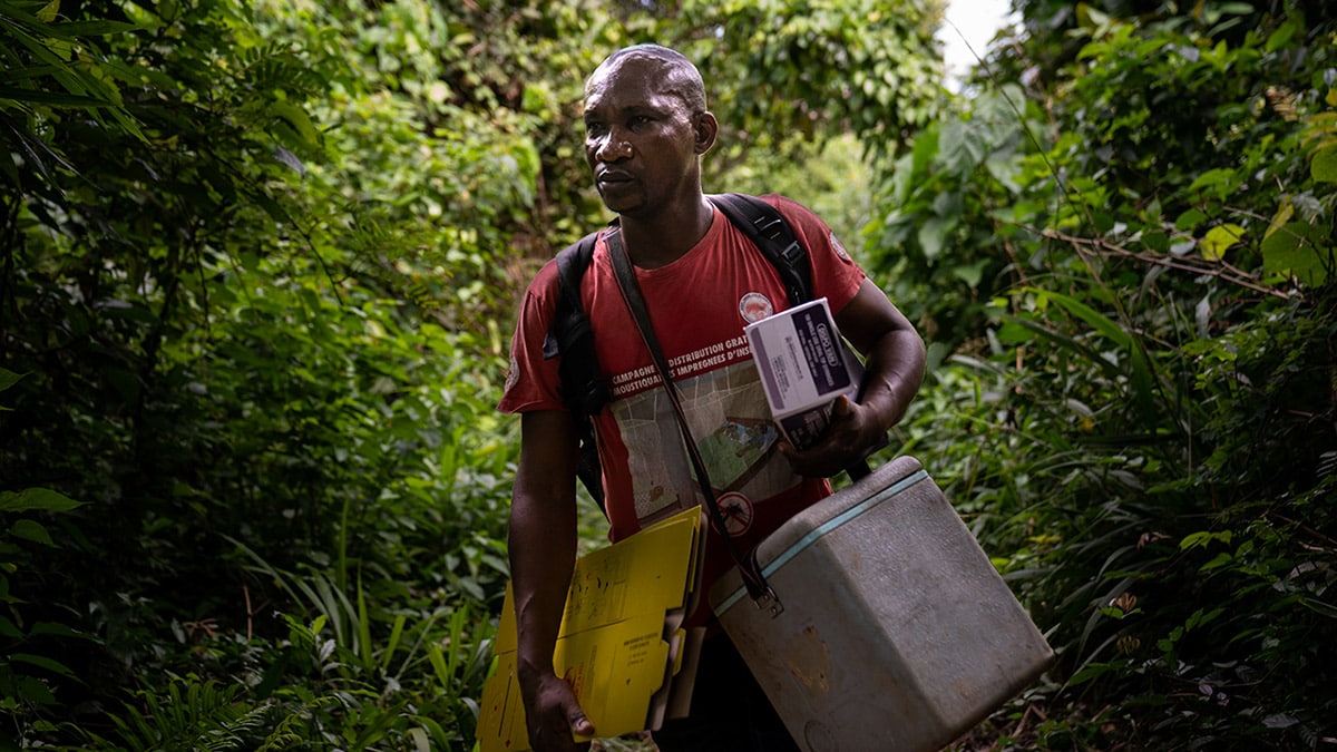 A male nurse carries vaccines and supplies along a jungle trail in Democratic Republic of the Congo.