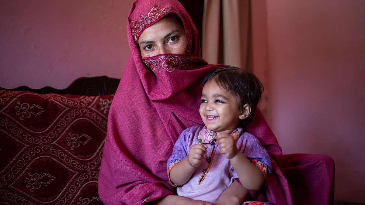 In a clinic, a mother sits with her smiling daughter in her lap.