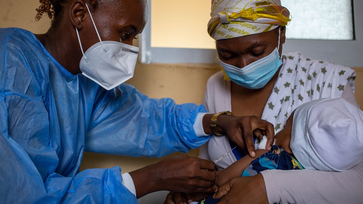 A nurse administers a vaccine to a baby held by another woman.