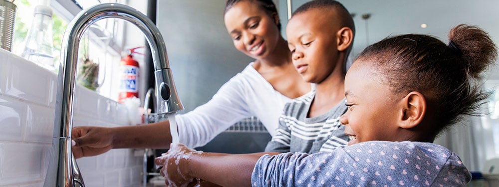 Family washing their hands together at the kitchen sink.