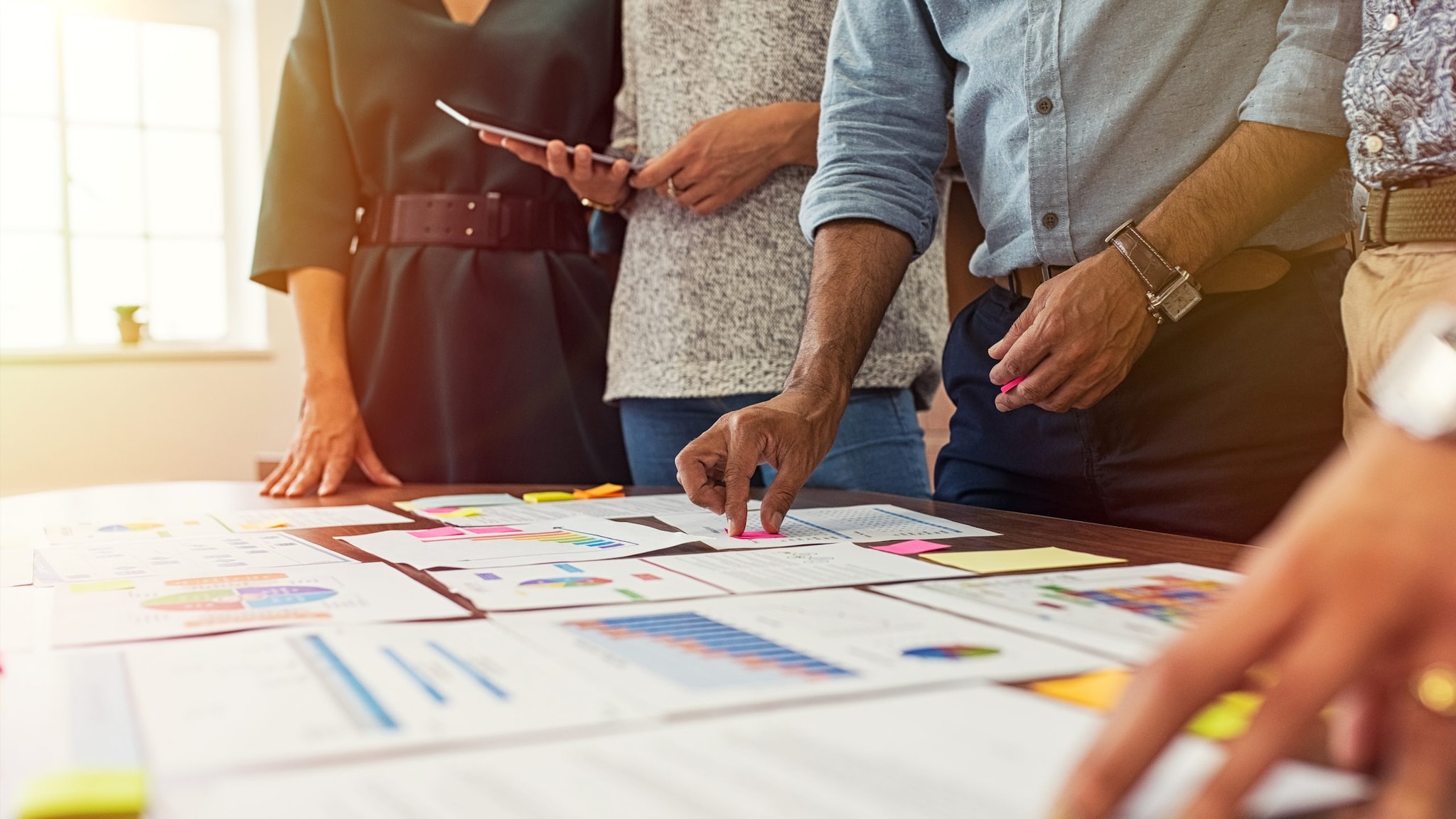 A group of people standing around a table with pieces of paper with charts and graphs.