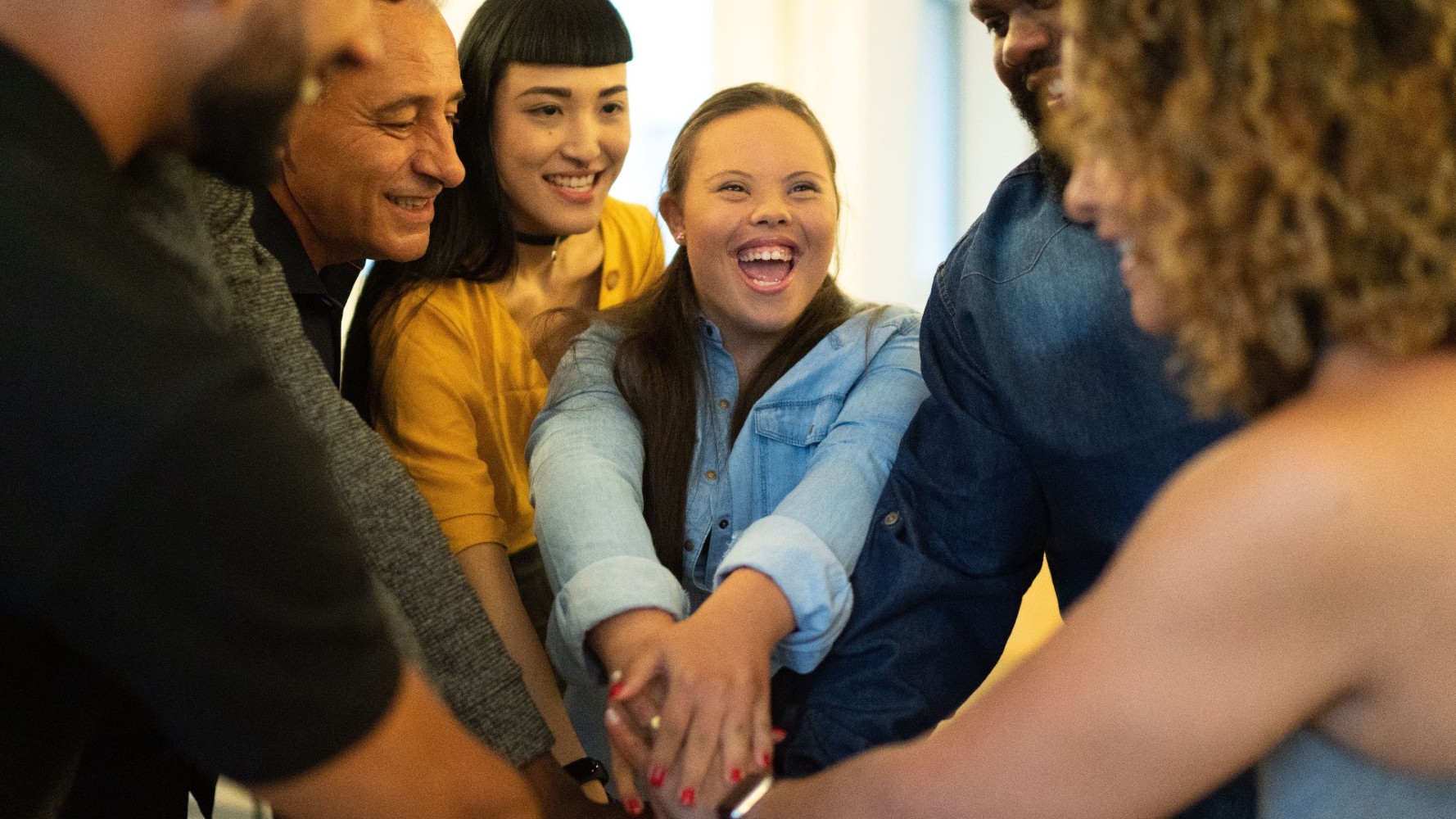 Group of diverse people smiling and reaching their arms together in a circle between them.