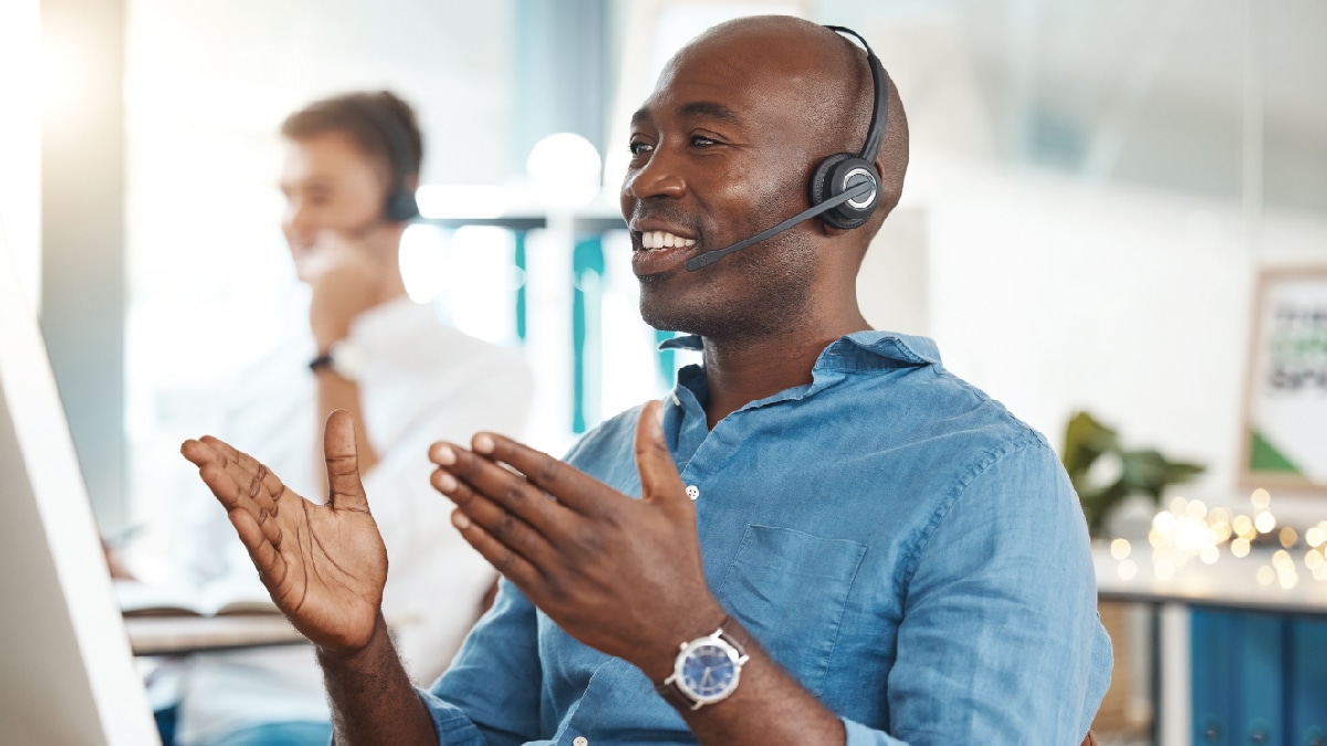 Picture of young, African American man at a computer with a phone headset on.