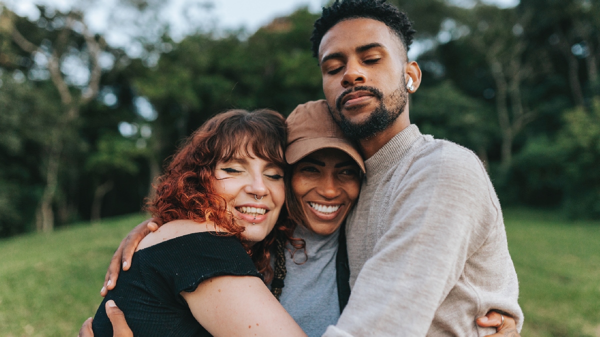 Three people standing in a field with their arms around each other.