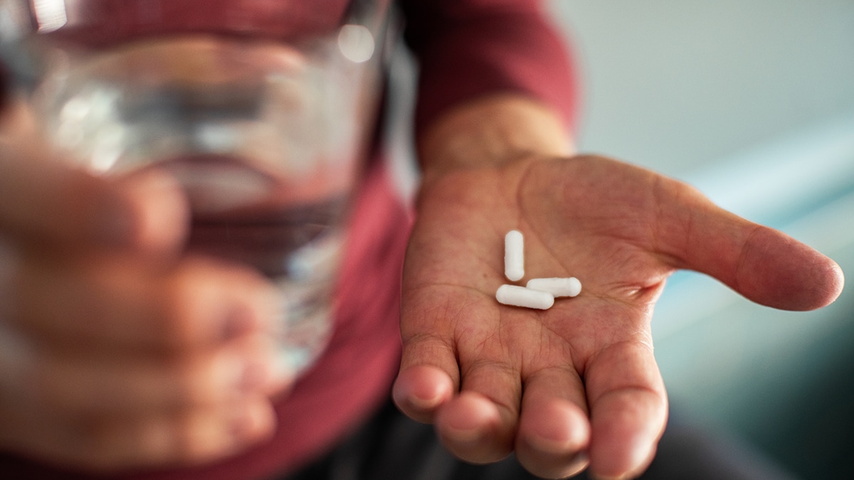 Image of a person holding a handful of mediation (pills) with a glass of water in the other hand.