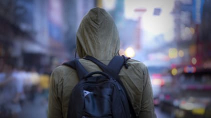 A view of the back of person wearing a backpack and a hooded sweatshirt outside in a cold busy urban setting.