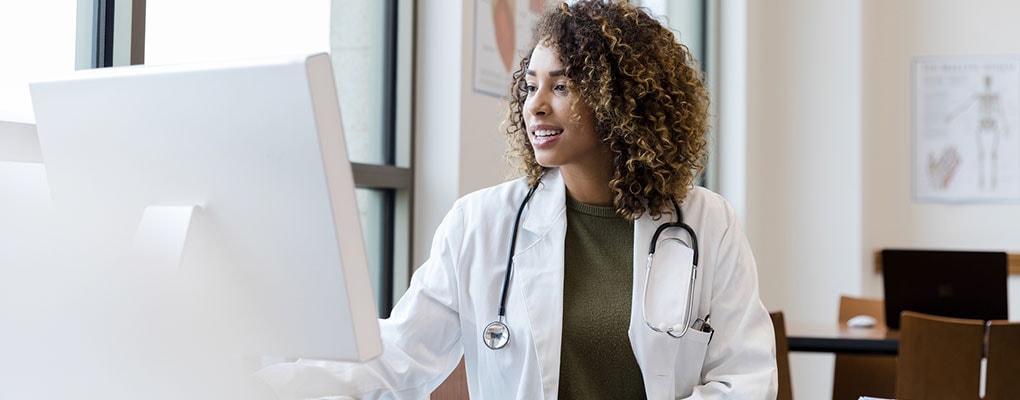 Adult female doctor reviews patient records on desktop PC.