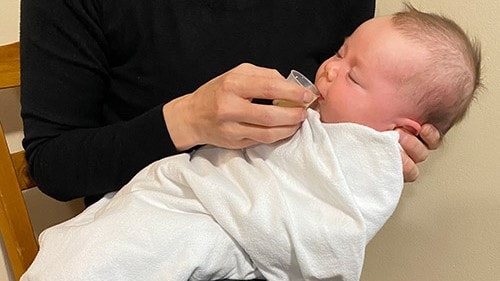 Caregiver cup feeding breast milk to a baby.