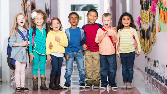 A group of 7 children standing in a school hallway, laughing and smiling at the camera. The boys and girls are 4 to 6 years.