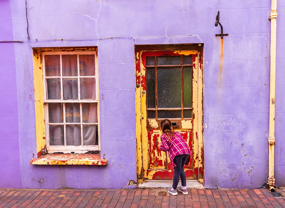 Little girl looking through mail slot of old weathered door.