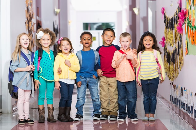 Young kids stand in a school hallway.