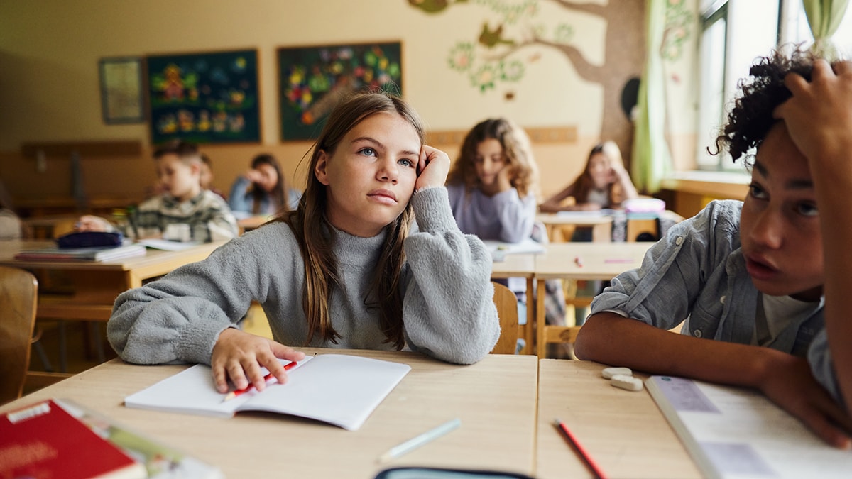 Tired schoolgirl attending a class with her classmates at elementary school.