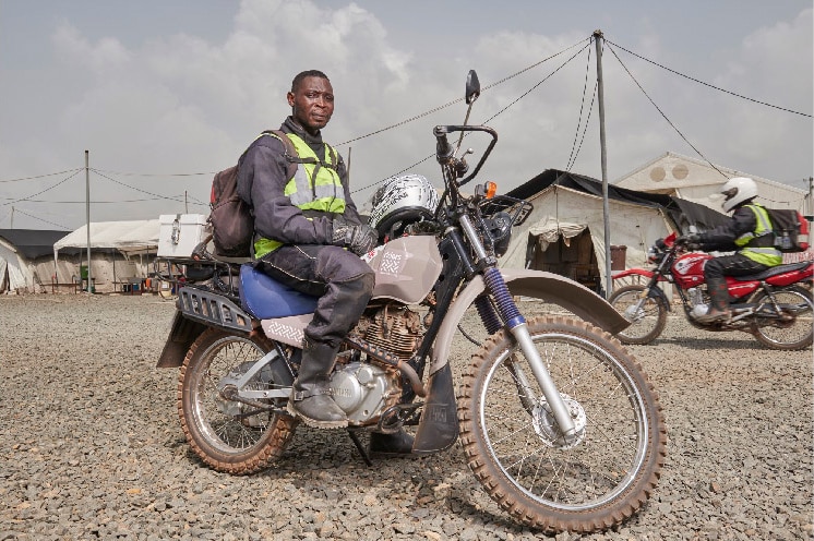 A motorcycle courier sitting on his motorcycle at a drop-off or pick-up location.