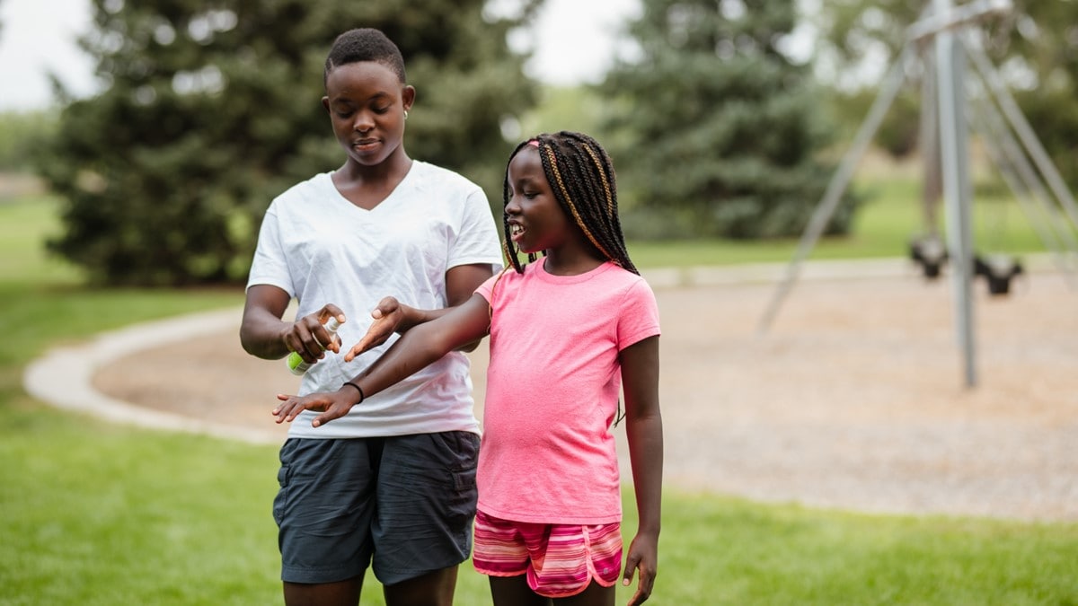 Photo showing an adult applying insect repellent to a child's arm.