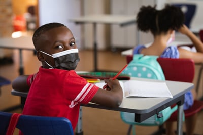 Boy wearing face mask at desk in elementary school