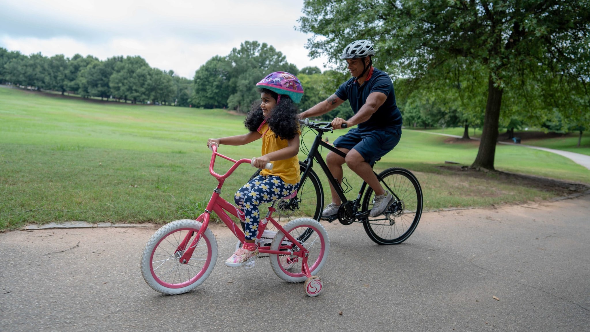 A father and daughter riding bikes in the park.