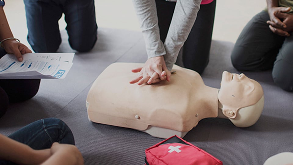 Group of people in a circle learning resuscitation with a mouth to mouth practice mannequin.