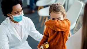 Healthcare worker with a mask, triaging a coughing child in a healthcare facility waiting room.