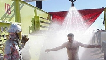 Firefighter using a portable shower attached to a firetruck to decontaminate a person