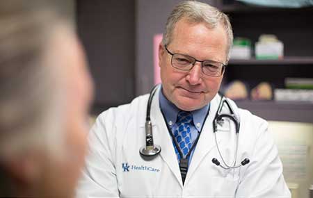 Dr. Timothy Mullett having a conversation with a patient. Dr. Mullett is wearing a white coat with a stethoscope placed around his neck.