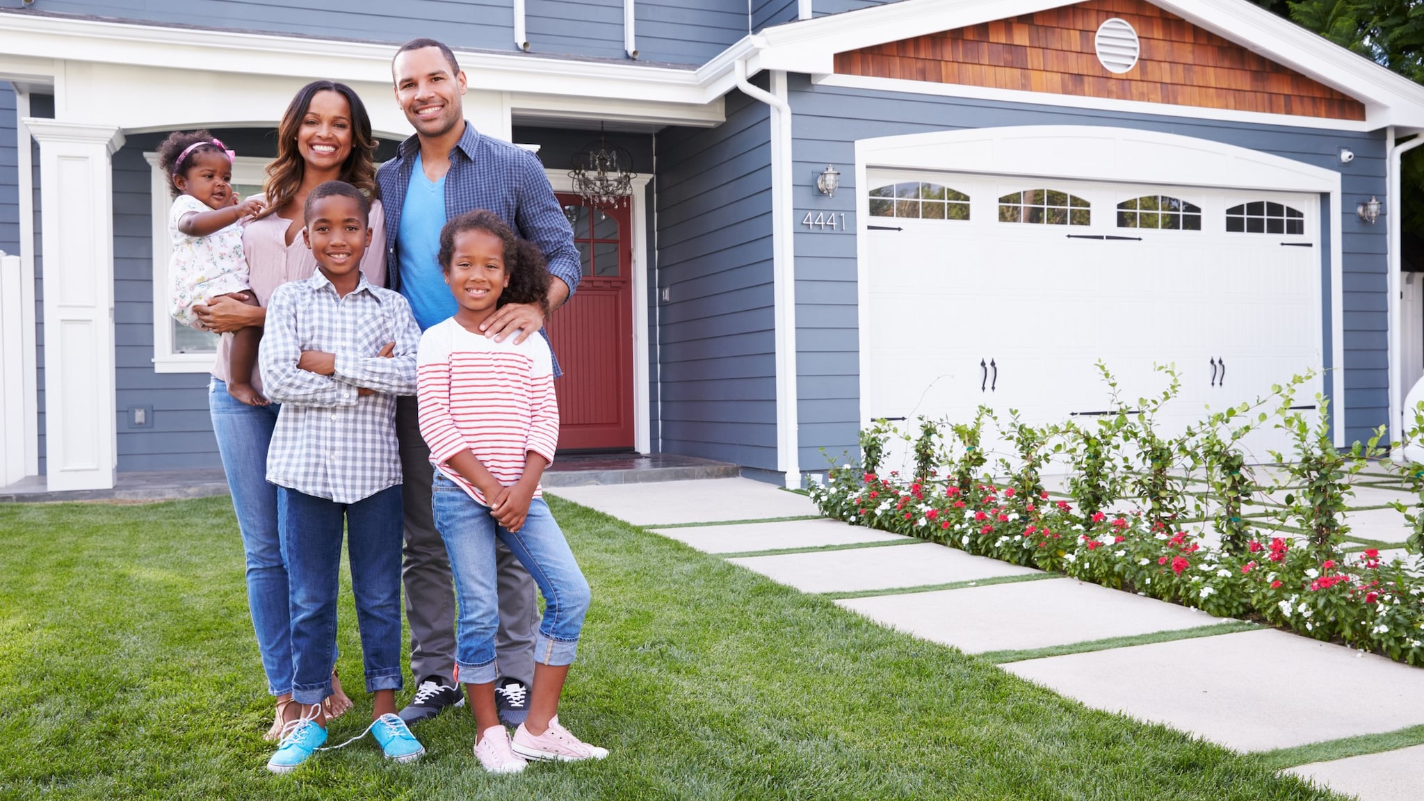 A happy family with young children standing outside their home smiling