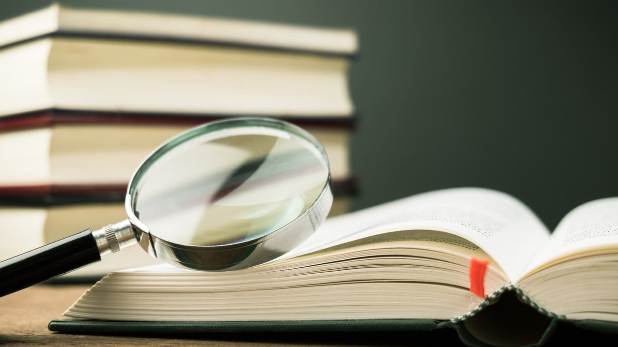 stack of books with a magifying glass