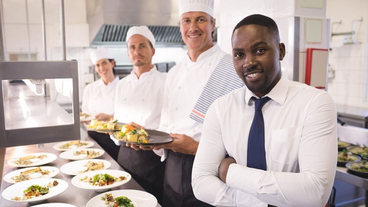 Kitchen manager with staff members in front of a counter full of plated food.