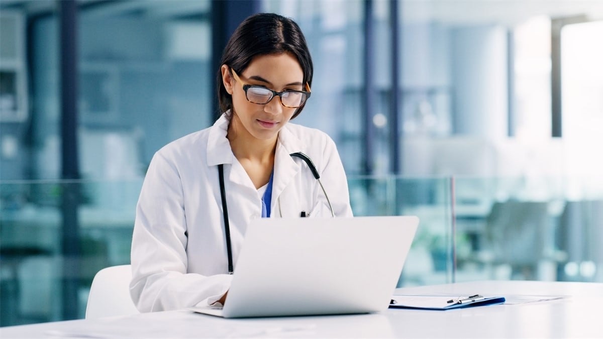 A healthcare professional at a desk reviews information on a notebook computer.