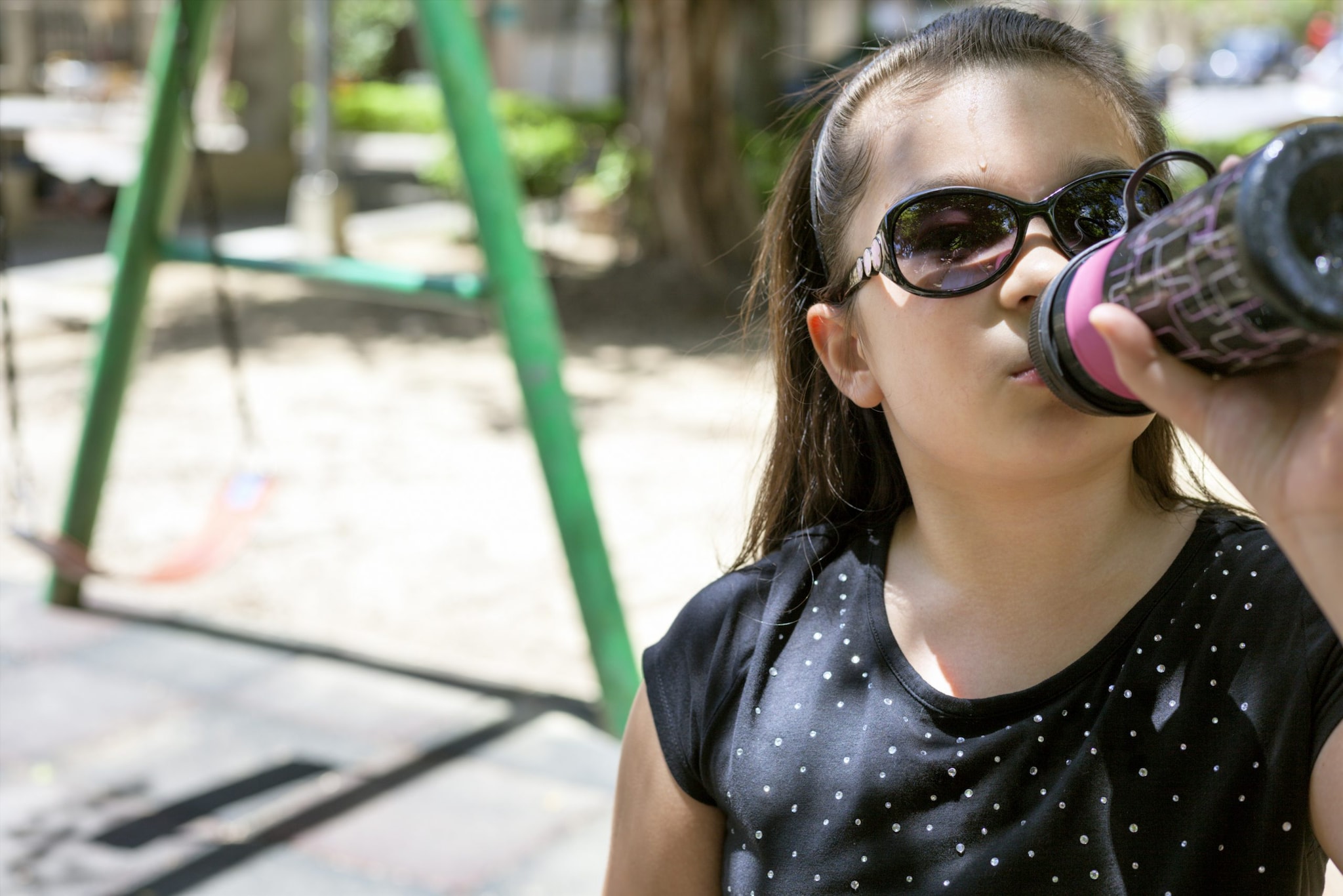 A young girl drinking from a water bottle in a playground.