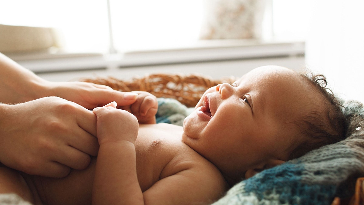 Smiling baby lying on back holding mom's fingers