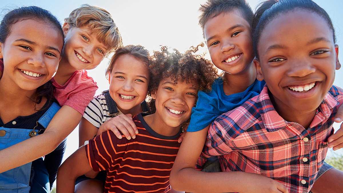 Diverse group of six kids piggybacking each other in the park.