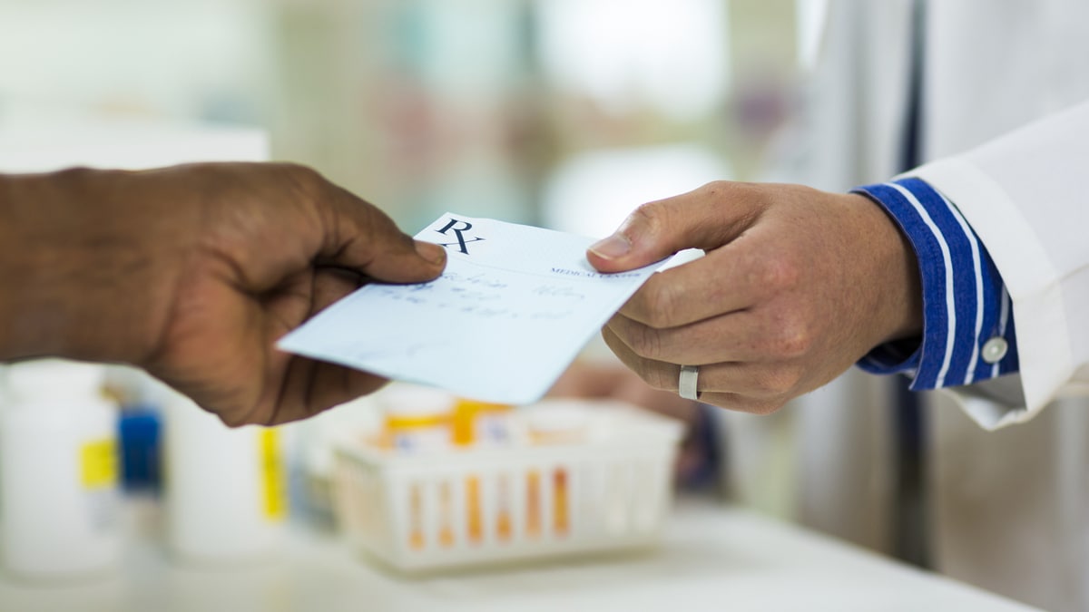 Photo of a person handing a prescription slip to a pharmacist.