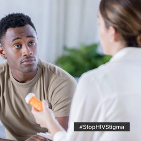 Image displays a medical provider holding a pill bottle while speaking to a male patient.