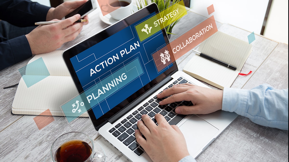 A person typing on a laptop. The laptop screen says, "Action Plan" Planning" "Strategy" and "Collaboration."