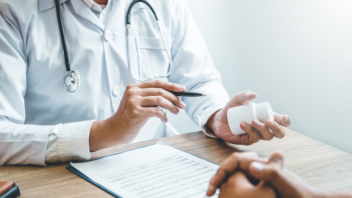 Doctor holding a white pill bottle and talking about medicine with a patient with no face visible