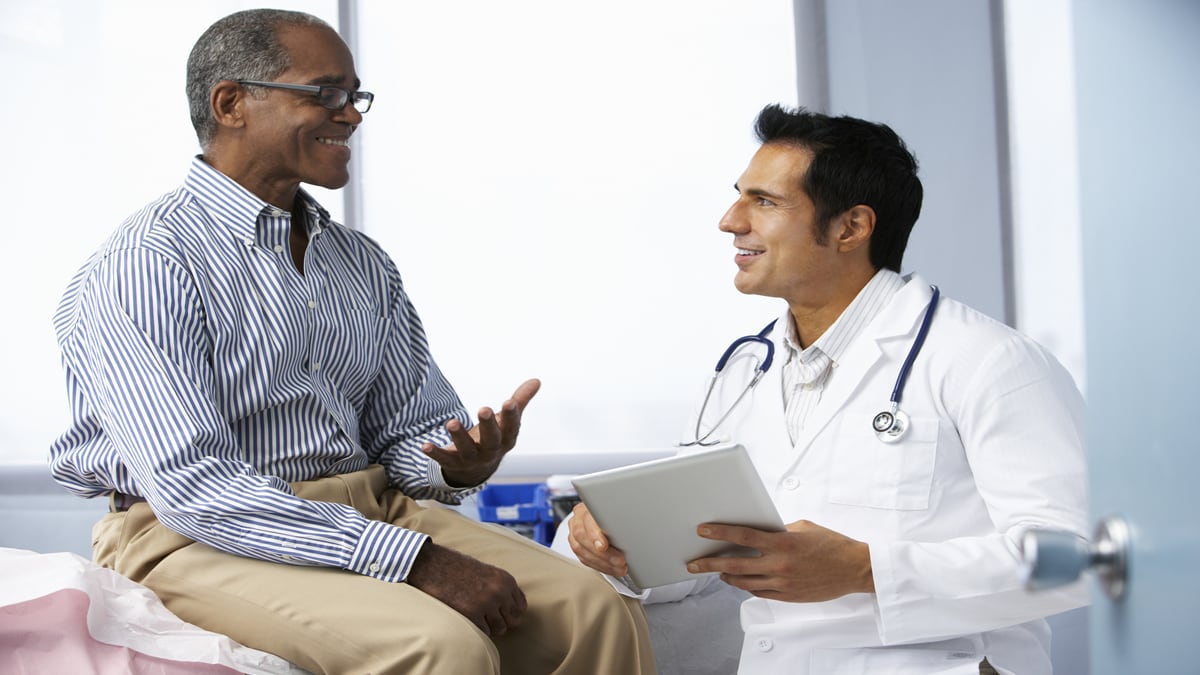 A patient sits on an exam table and discusses health with a health care provider.